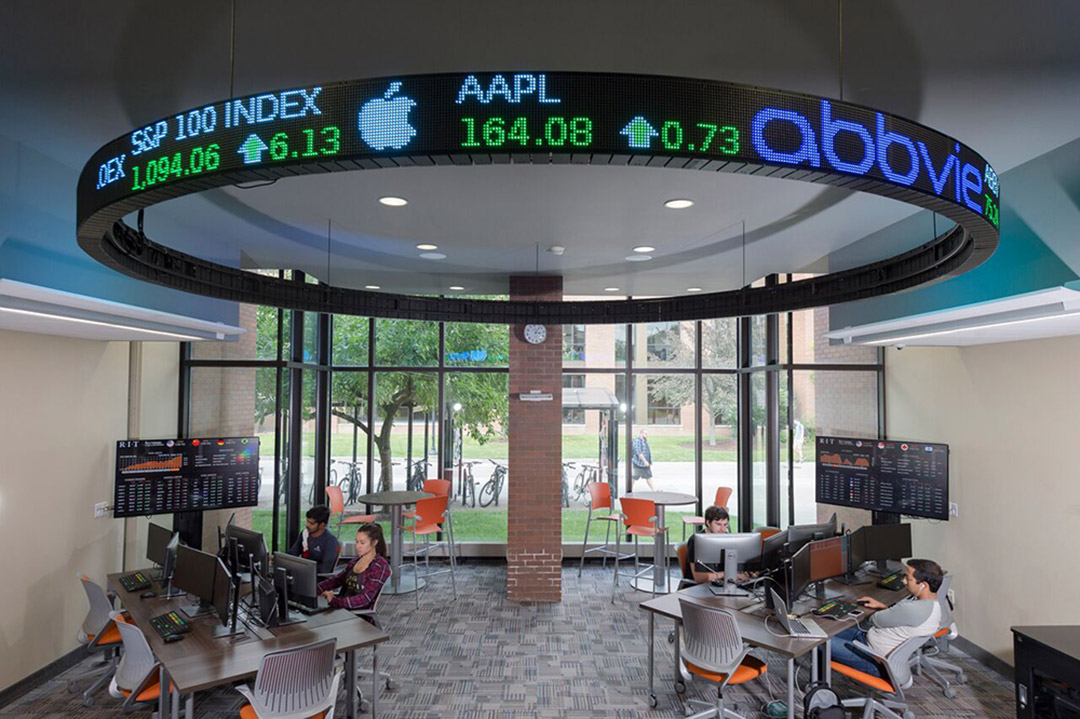 room with computer stations and large digital stock ticker display.