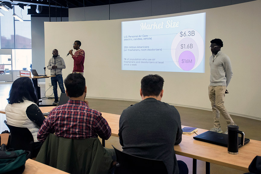 three students standing in front of room giving presentation.