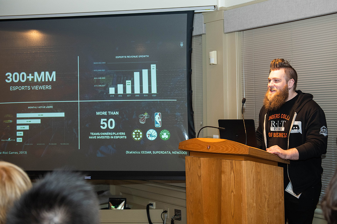 Man stands at podium with PowerPoint presentation displayed on screen next to him