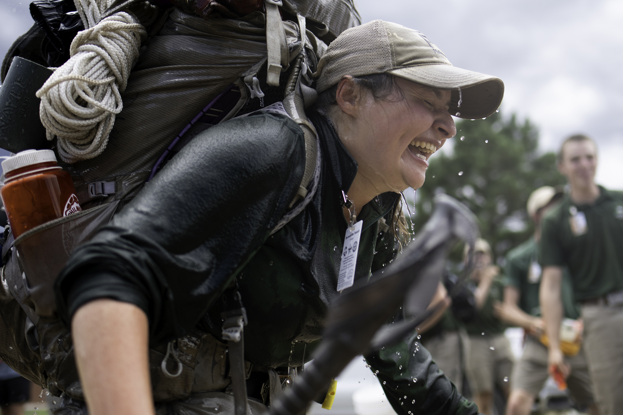 A woman is drenched while hiking with a lot of gear.