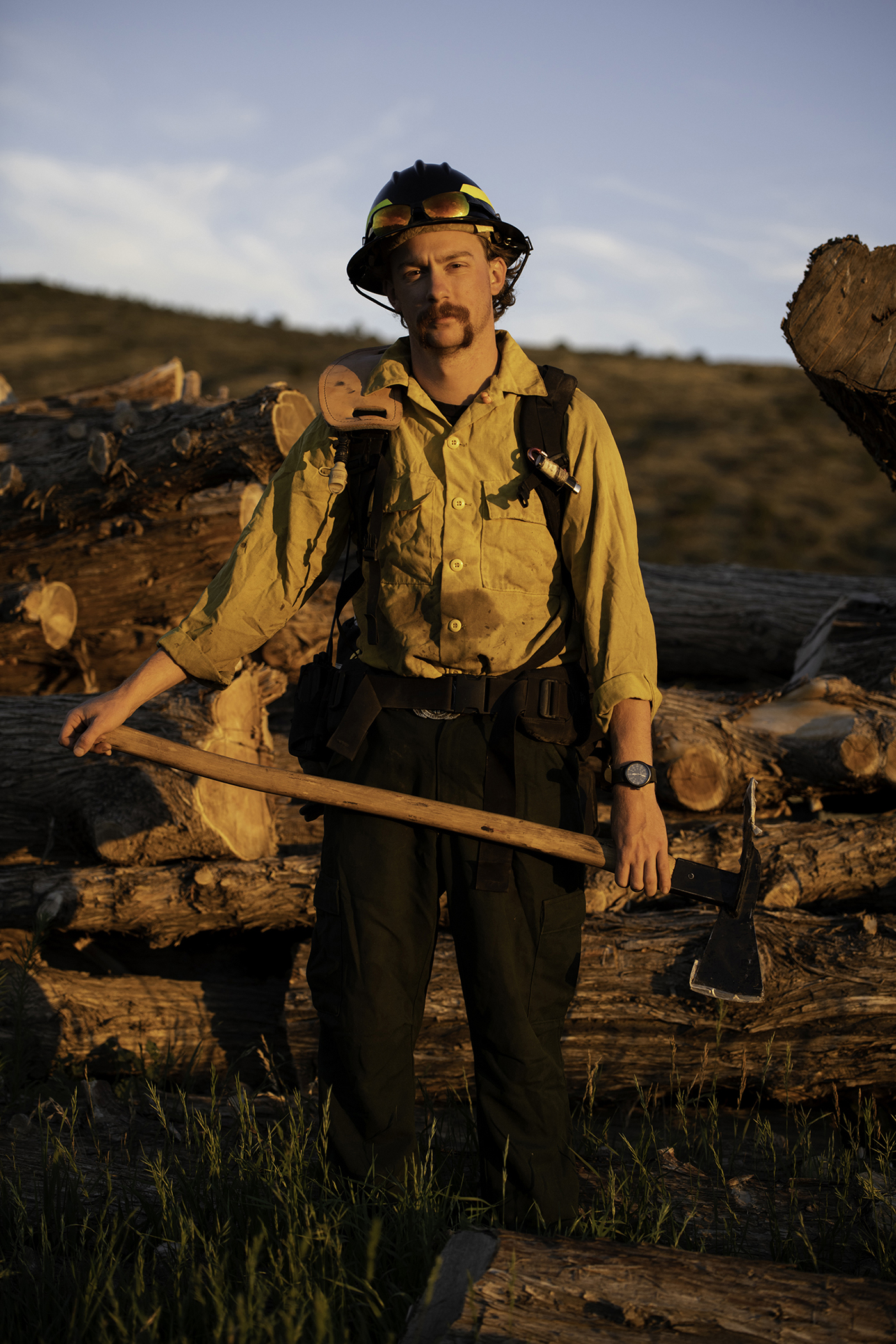 A portrait of a man in the wild, surrounded by chopped-down lumber.