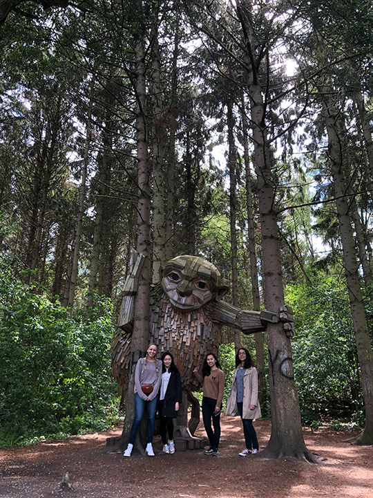 Students stand in forest with statue of giant.