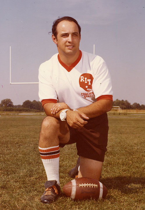 Football player kneels next to ball in 1960s.