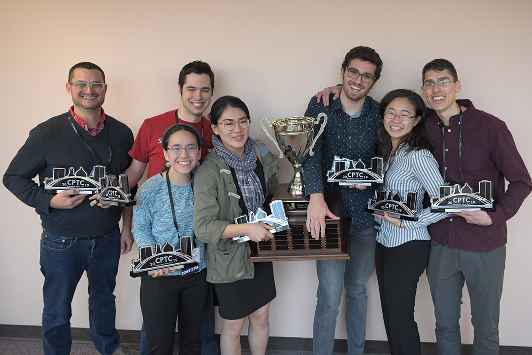 Team of seven students stands with trophies.