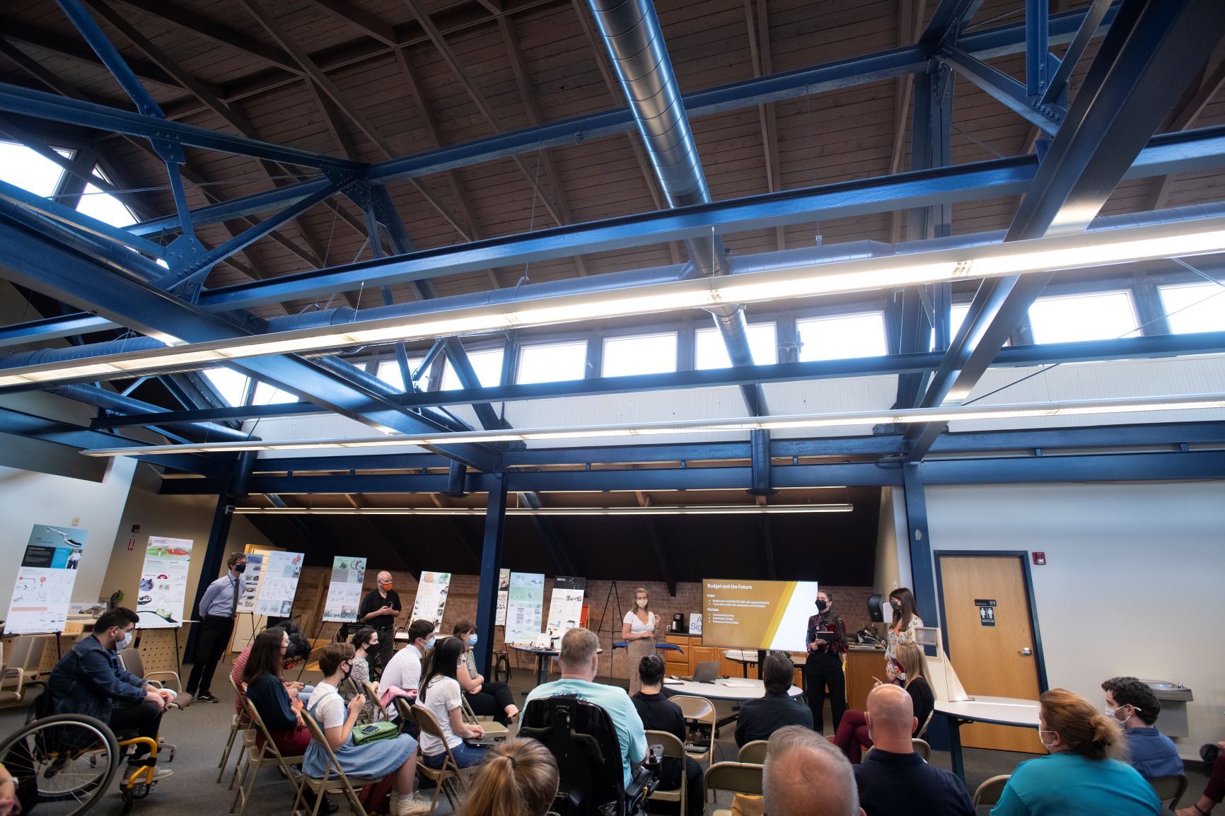 A roomful of people watch a person presenting in front of a screen.