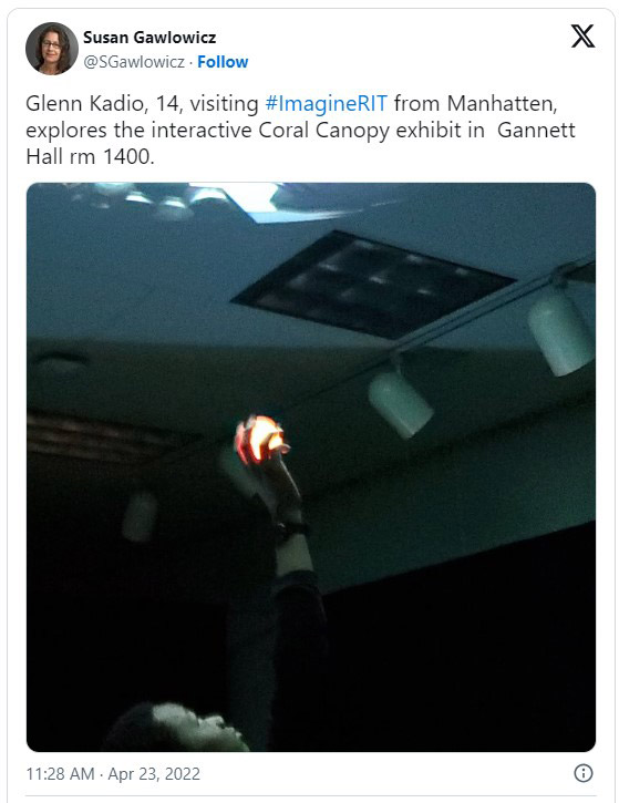 Tweet from Susan Gawlowicz on April 23, 20 22, with a photo of a person holding a glowing ball up to a ceiling and the text, Glenn Kadio, 14, visiting Imagine R I T from Manhattan, explores the interactive Coral Canopy exhibit in Gannett Hall room 1400.