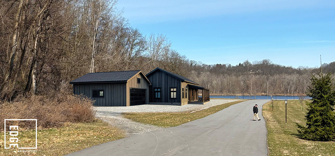a brown building sits on the left of an image next to an empty road with a pond in the background.