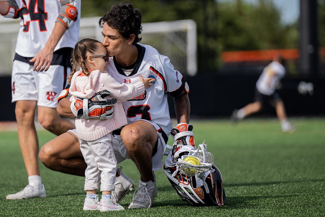 college lacrosse player kissing a little girl on the forehead.
