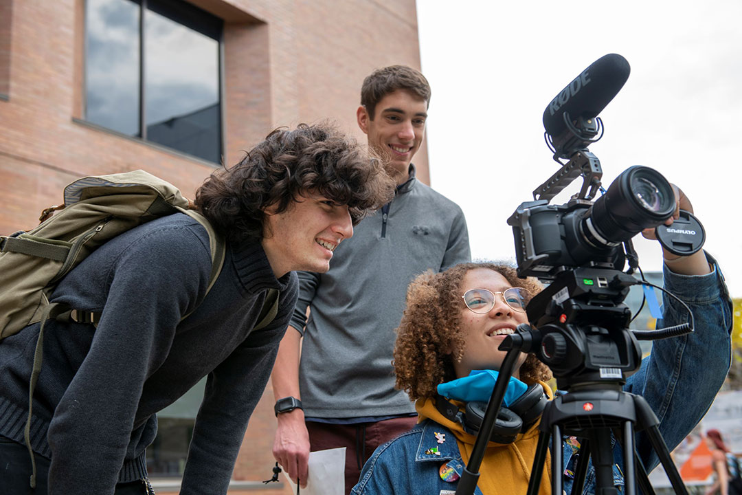 three college students using a camera on a tripod.