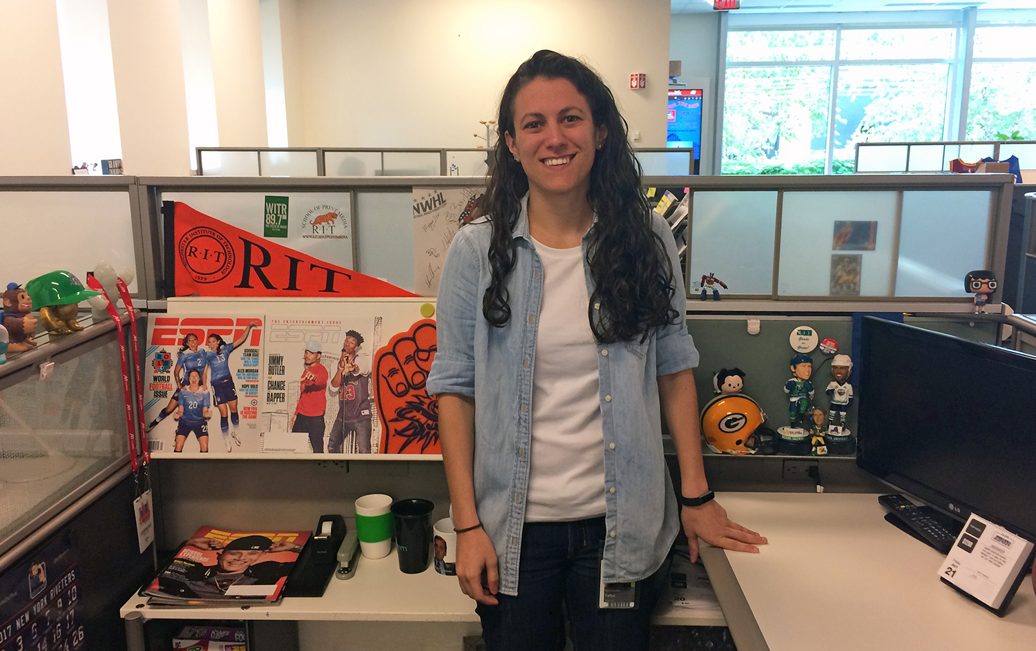Fallon standing in her cubicle which features RIT branded items