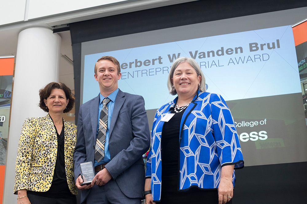 Student holding award stands between dean and provost.