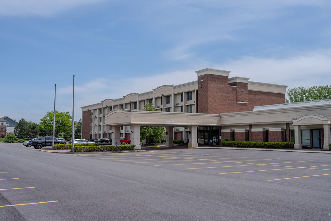 Exterior of a hotel building with covered entry and empty parking lot.