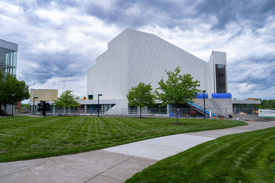 Modern building under construction with white geometric facade and green lawn.
