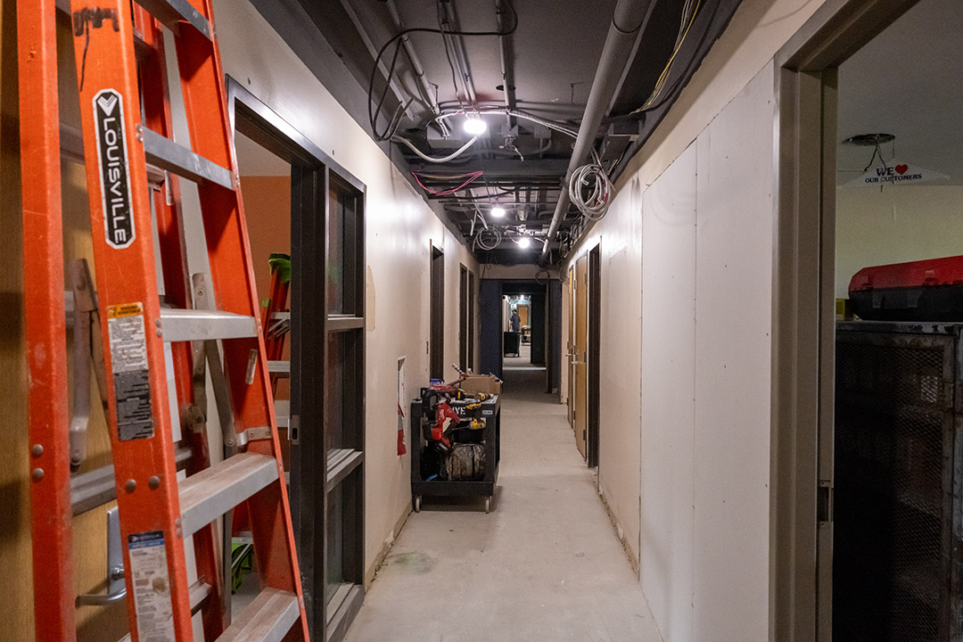 Construction hallway with exposed ceiling pipes, tools, and a ladder.