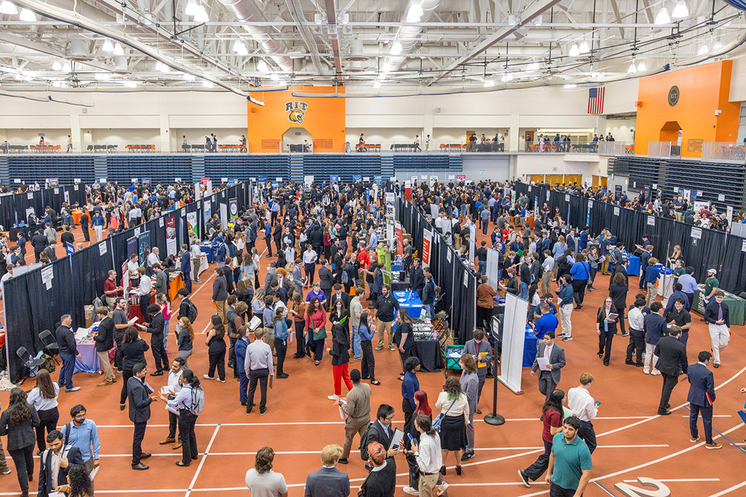 a crowded gymnasium space filled with tables for a career fair.