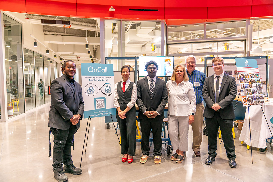 students stand together in front of a presentation board in an open area at R I T.