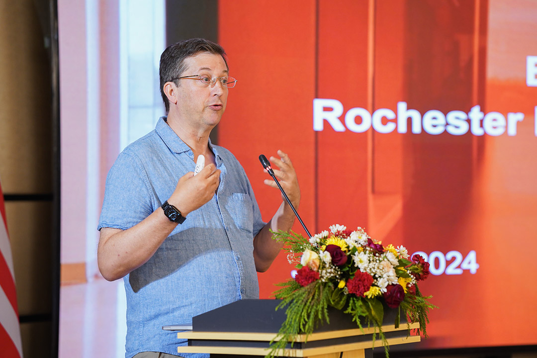 a man stands at a podium speaking to attendees.