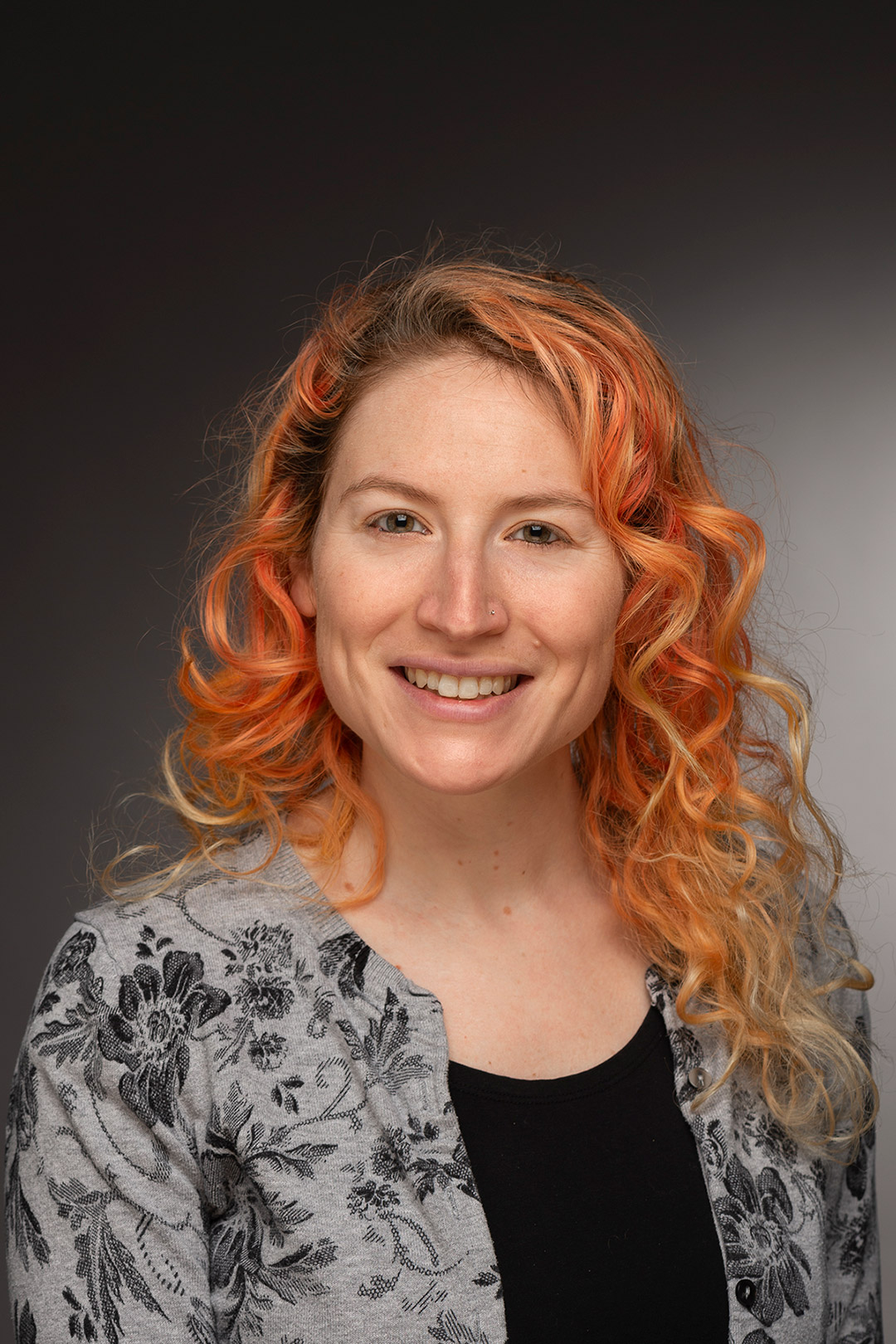 a woman with red curly hair sits for a headshot.