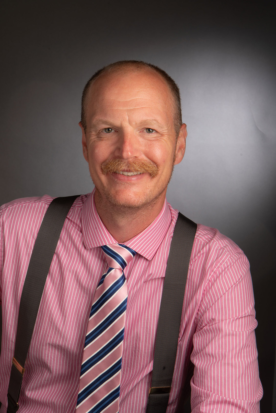 Billy Brumley appears in a headshot with a pink shirt, striped tie, and dark suspenders.