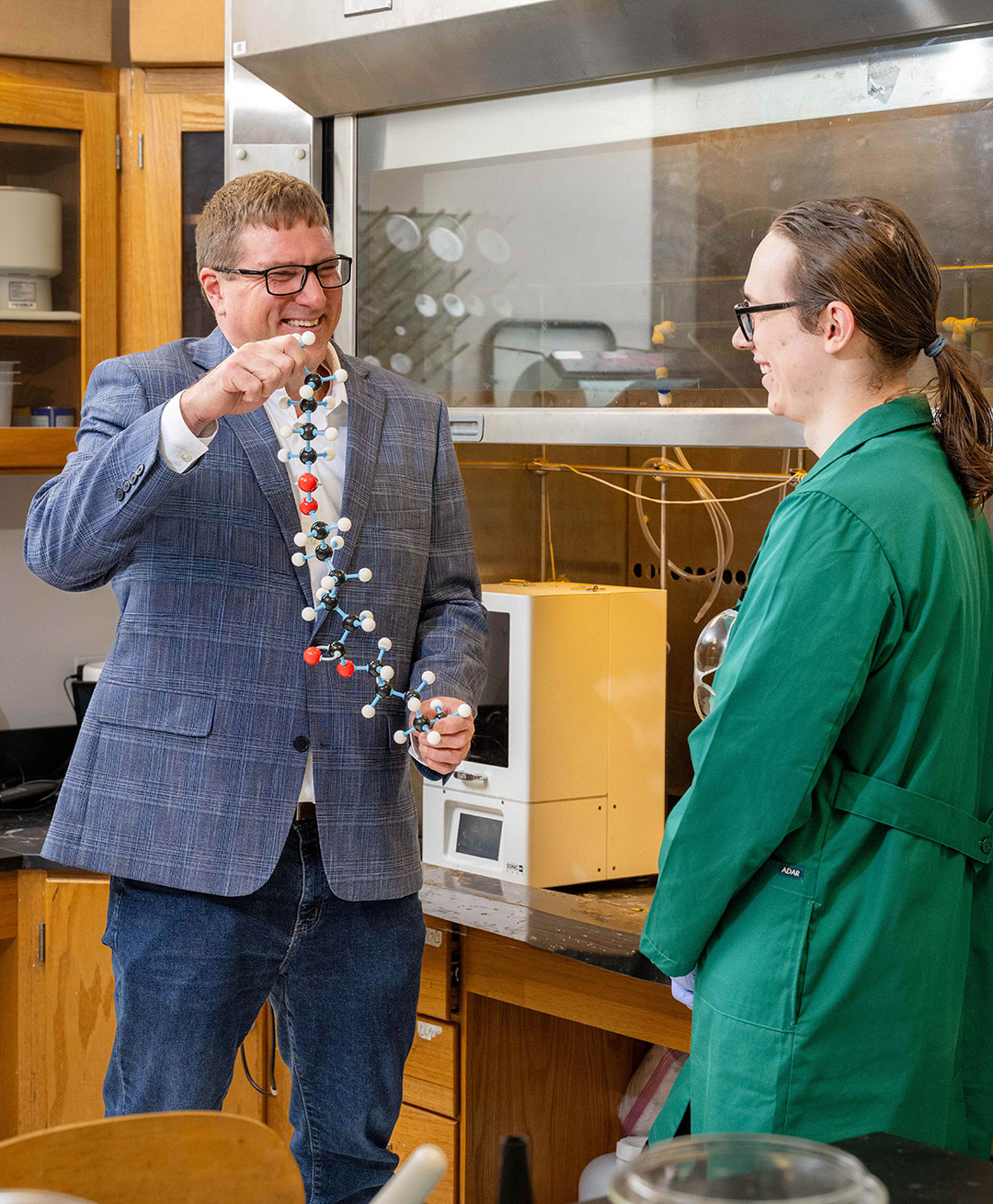 a man in a gray suit shows a polymer structure to a student.