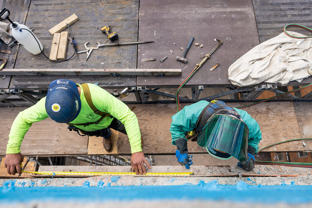 two men in construction hats work on the side of a brick residence hall