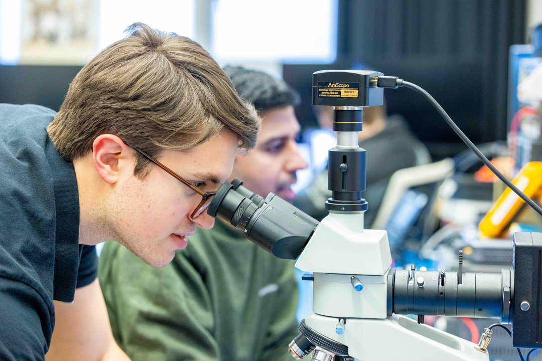 a ale student looks through a microscope in a computer lab