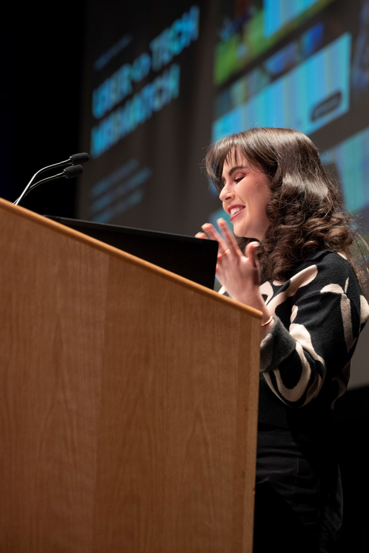 a woman stands at a podium addressing a crowd.