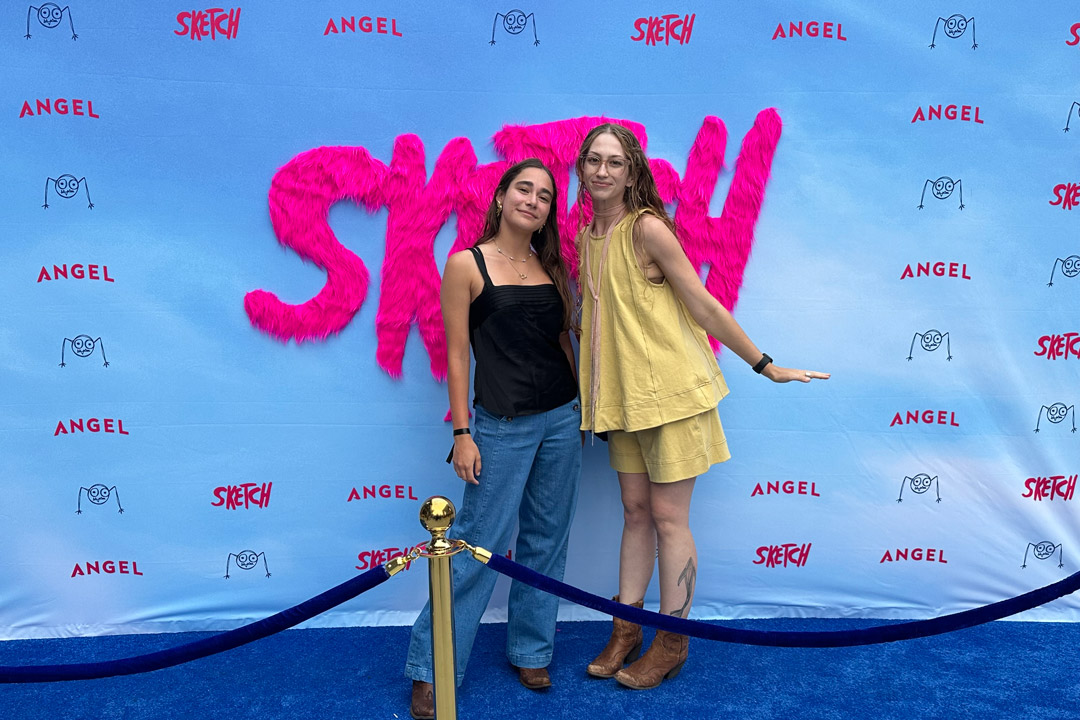 two young women stand in front of a step and repeat at a movie premiere