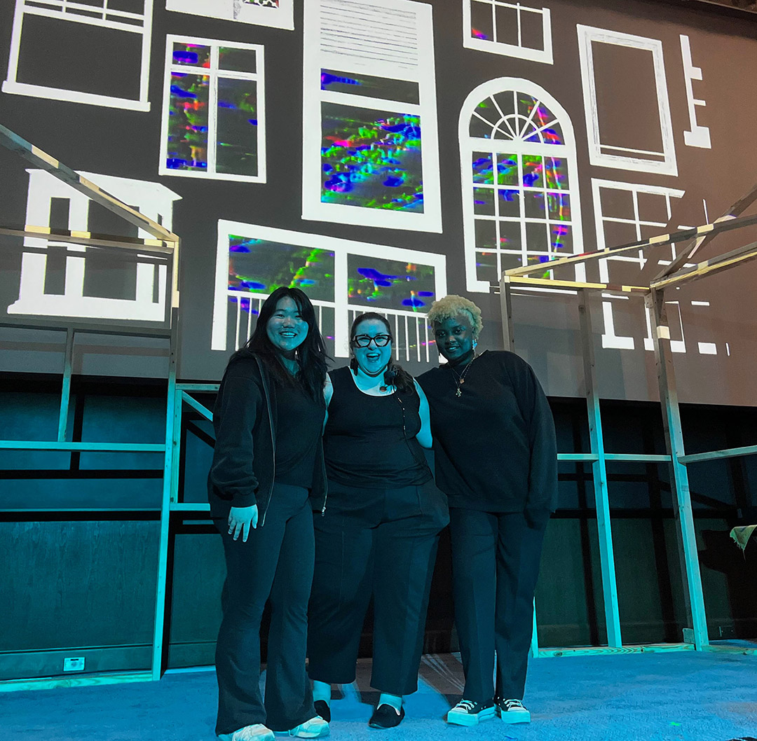 three people stand on stage smiling.