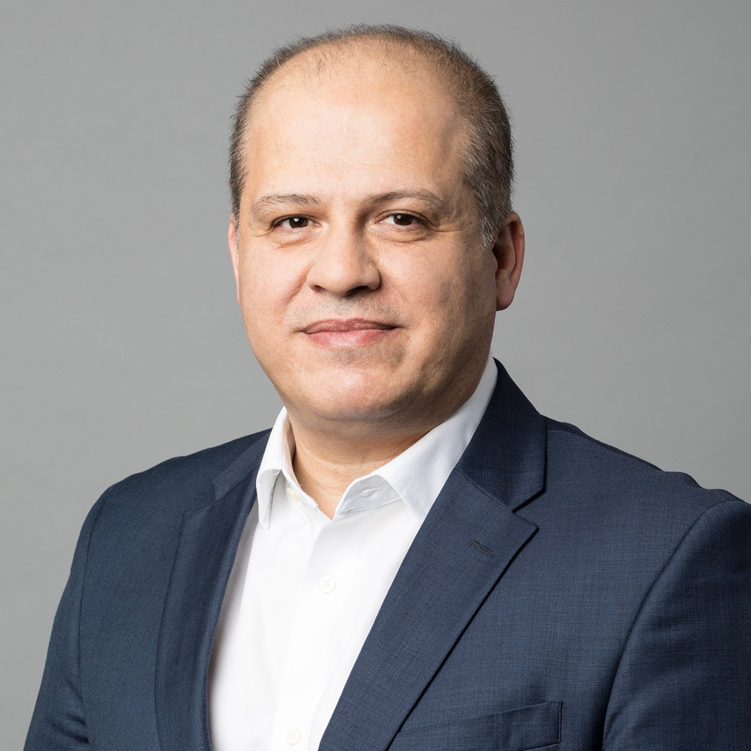 Man in a dark suit and white shirt against a gray background