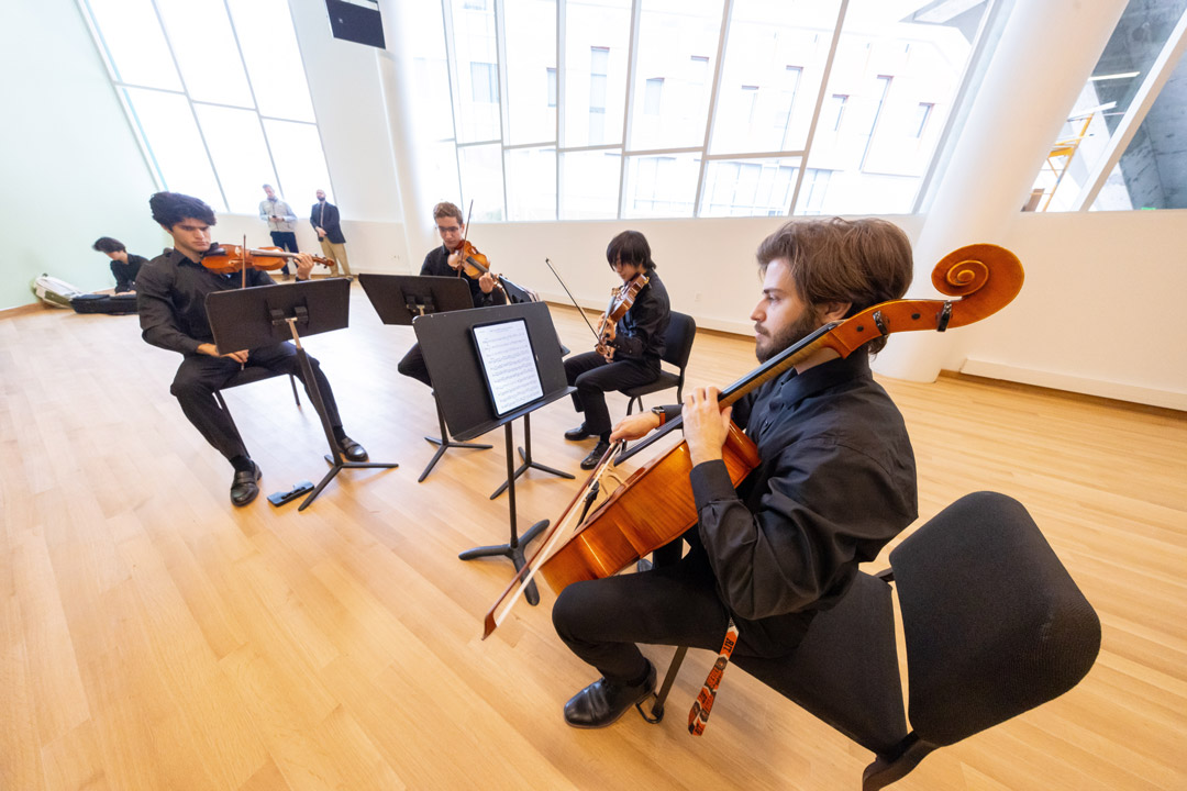 three students practice instruments in a brightly lit room