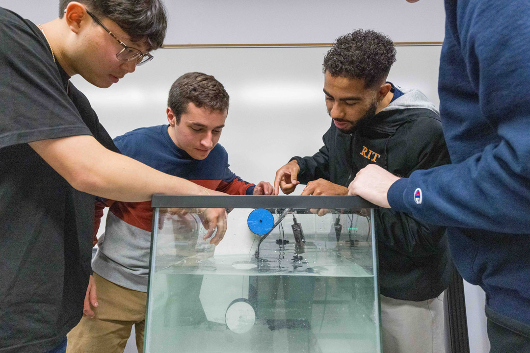 a group of students submerge a robot car in to a fish tank to test the underwater capacity.