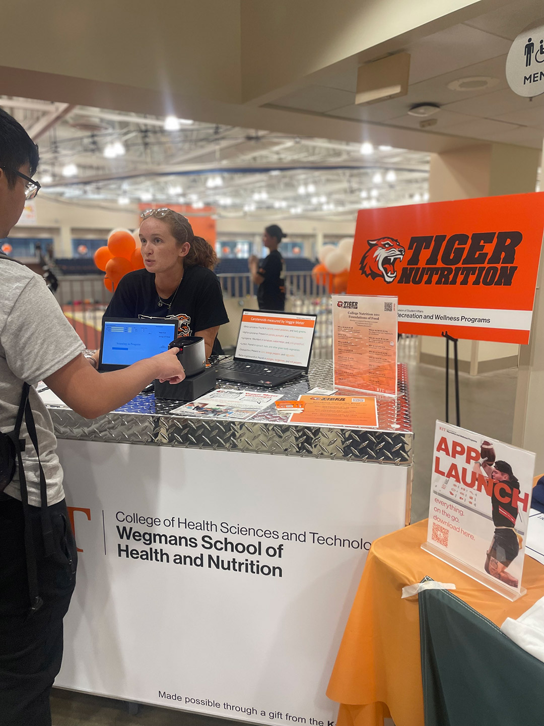 a college age irl stands behind a table labeled as Tiger Nutrition speaking to people that stop by.