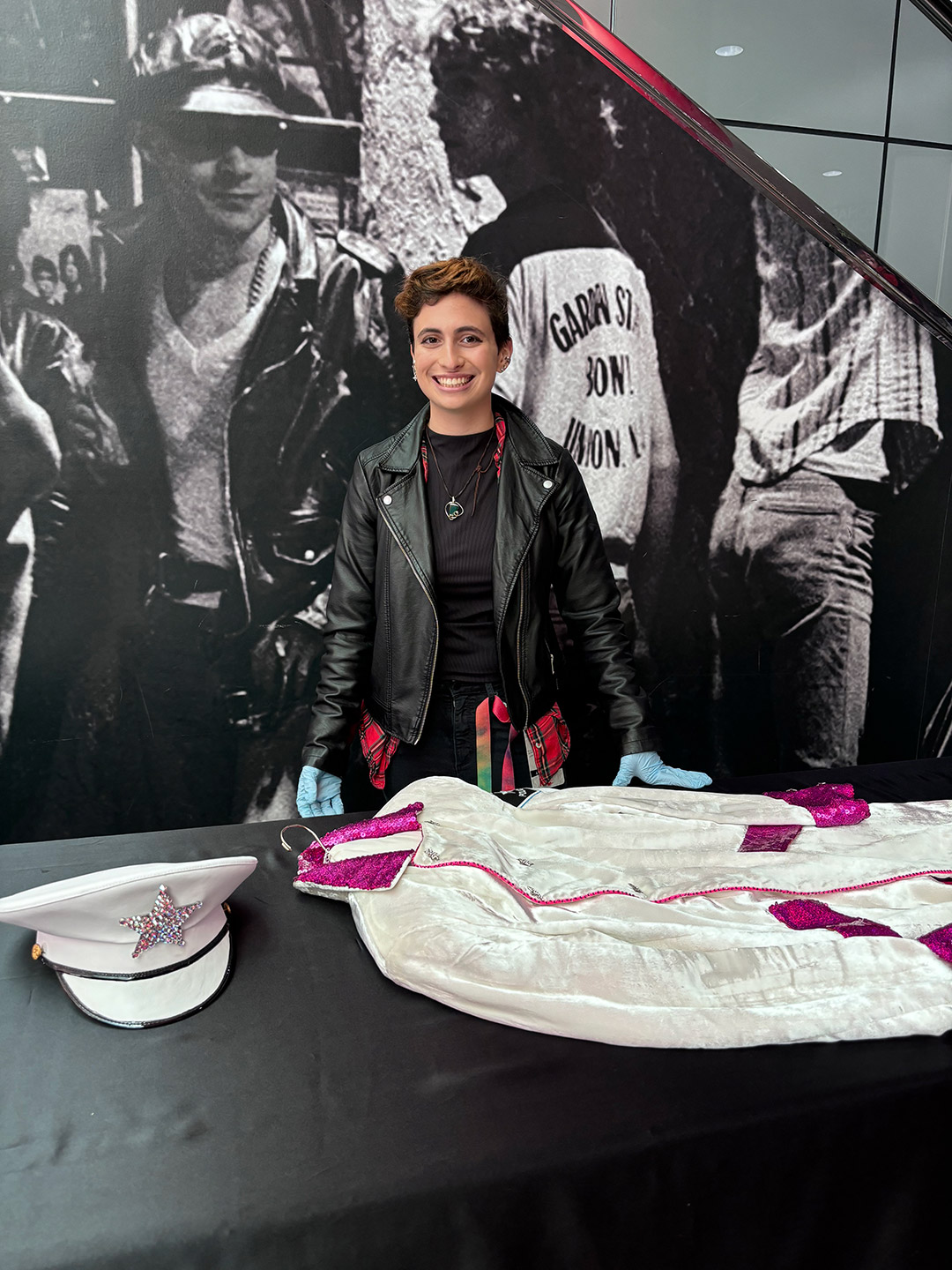 a woman with short dark hair leans over a lightbox on a table looking at slides in a research repository. In the foreground, the pelt of a tiger is resting on the table.