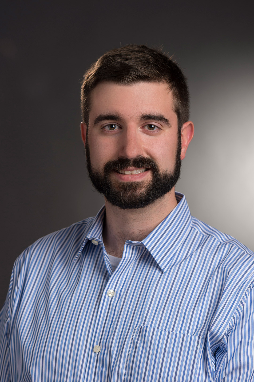 a photo of a young man with dark hair in a blue button down dress shirt.