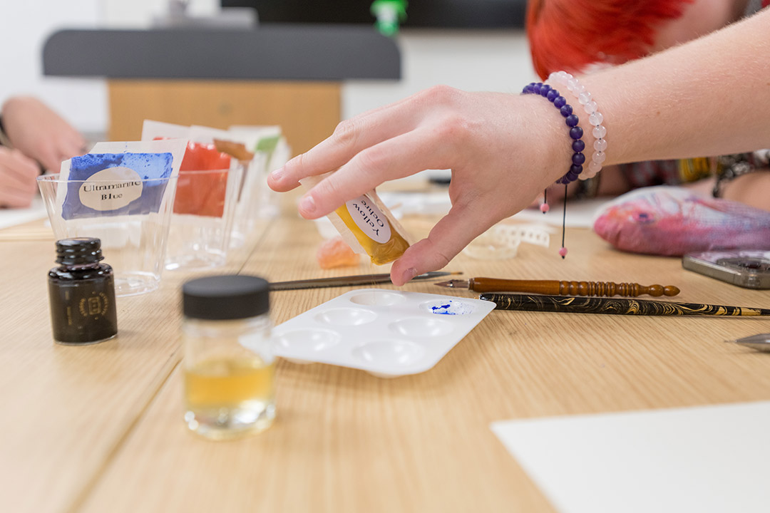hands hold packets of pigments above a table.