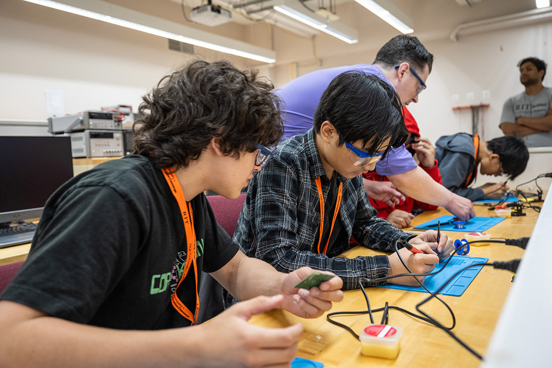 Students solder a circuit board during the Chip Experience immersion. In the background, Jason Hoople, a lecturer in the electrical and microelectronic engineering department, works with another student. 