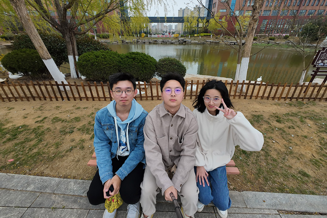 Three students from RIT China are shown sitting on a bench in front of a pond.