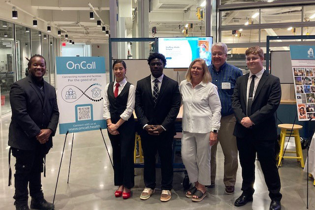 students stand together in front of a presentation board in an open area at R I T.