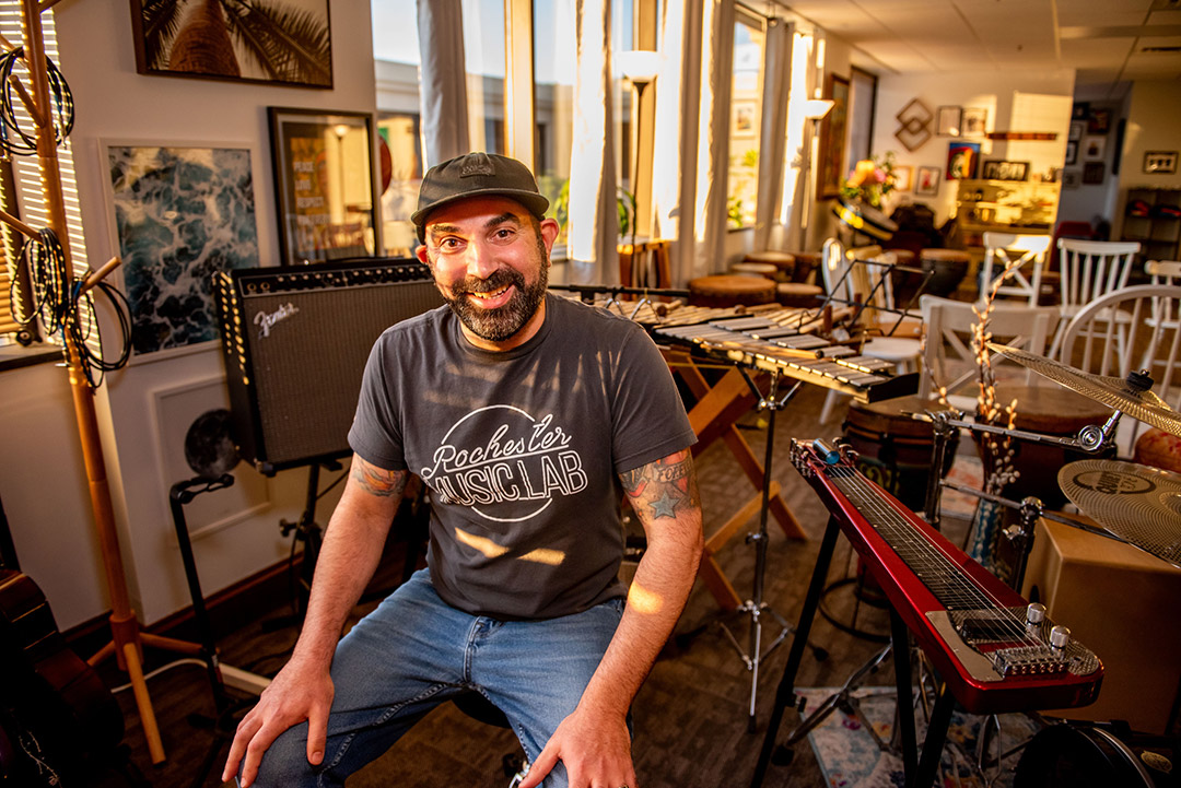 a man sits in a room full of musical instruments.