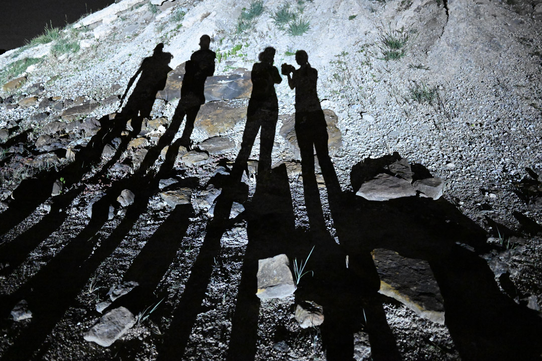 People cast long shadows on rocky ground at night.