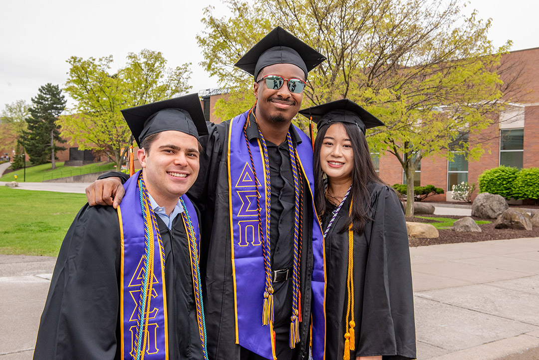 three students gather for a photo, dressed in graduation regalia.