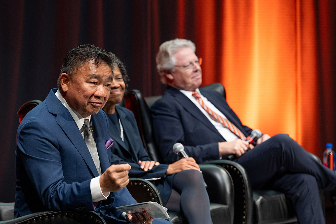 a man leans forward in his chair as a part of an on-stage panel answering a quetions from an audience member