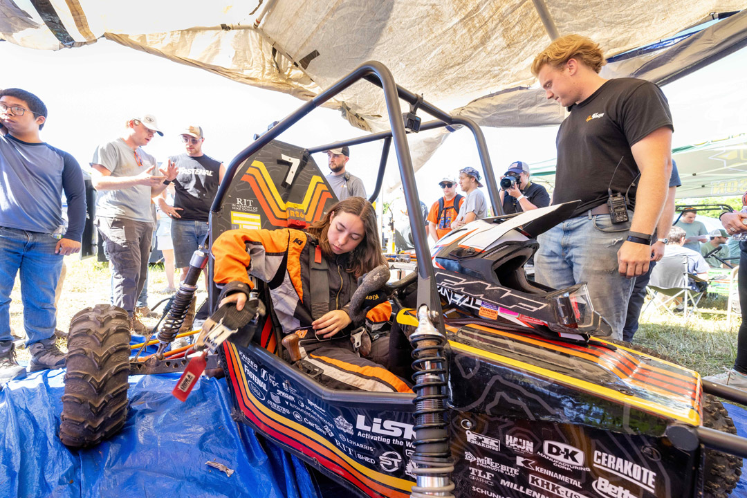 Student driver prepares to enter Baja SAE off-road vehicle during competition.