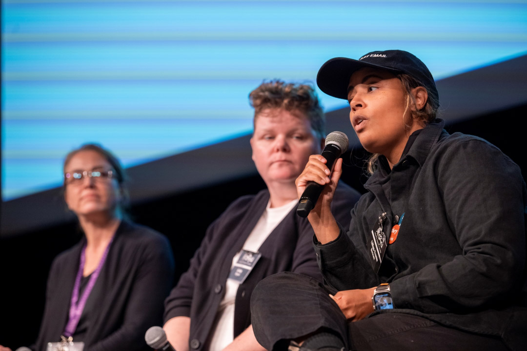 a woman sits next to two other people on a stage, holding a mic.