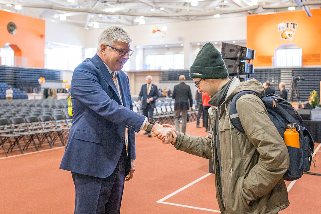 William Sanders shares a handshake with a college age male student.