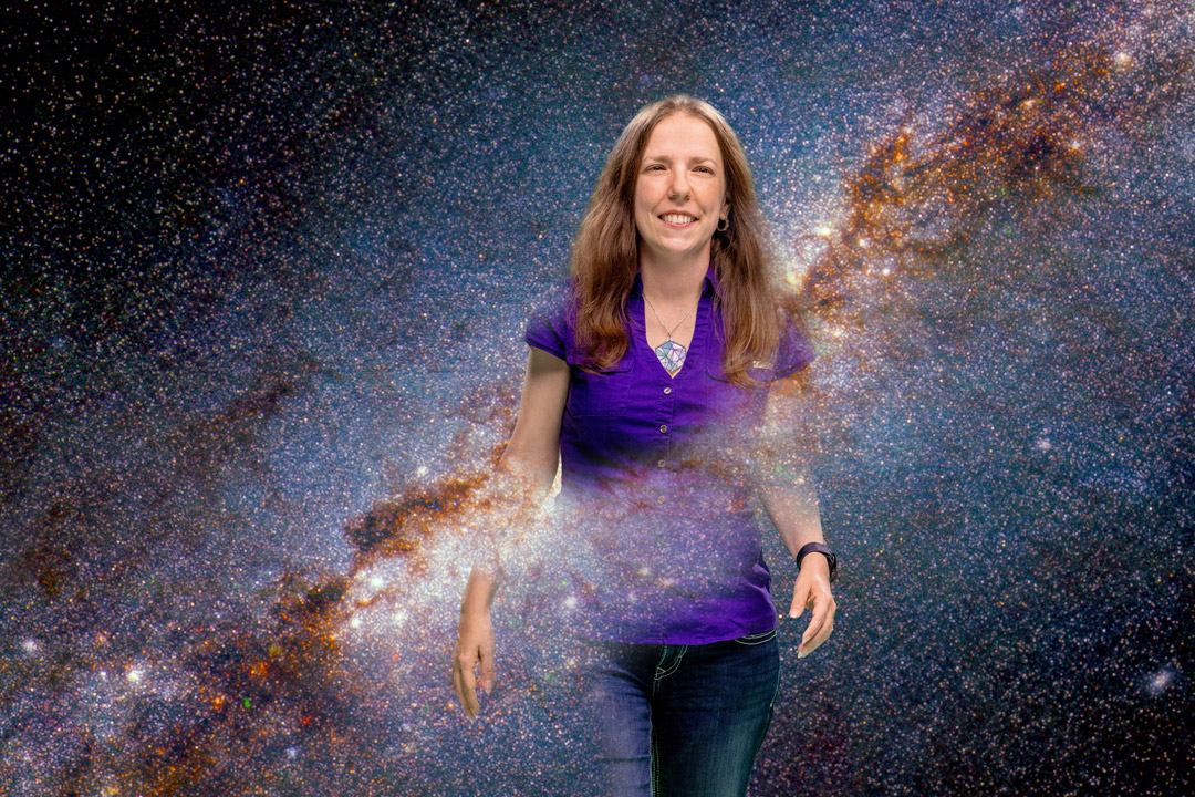 a woman stands in a purple shirt with the cosmos behind her
