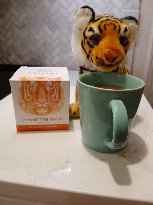 a stuffed tiger sits next to a mug of tea on a small table.