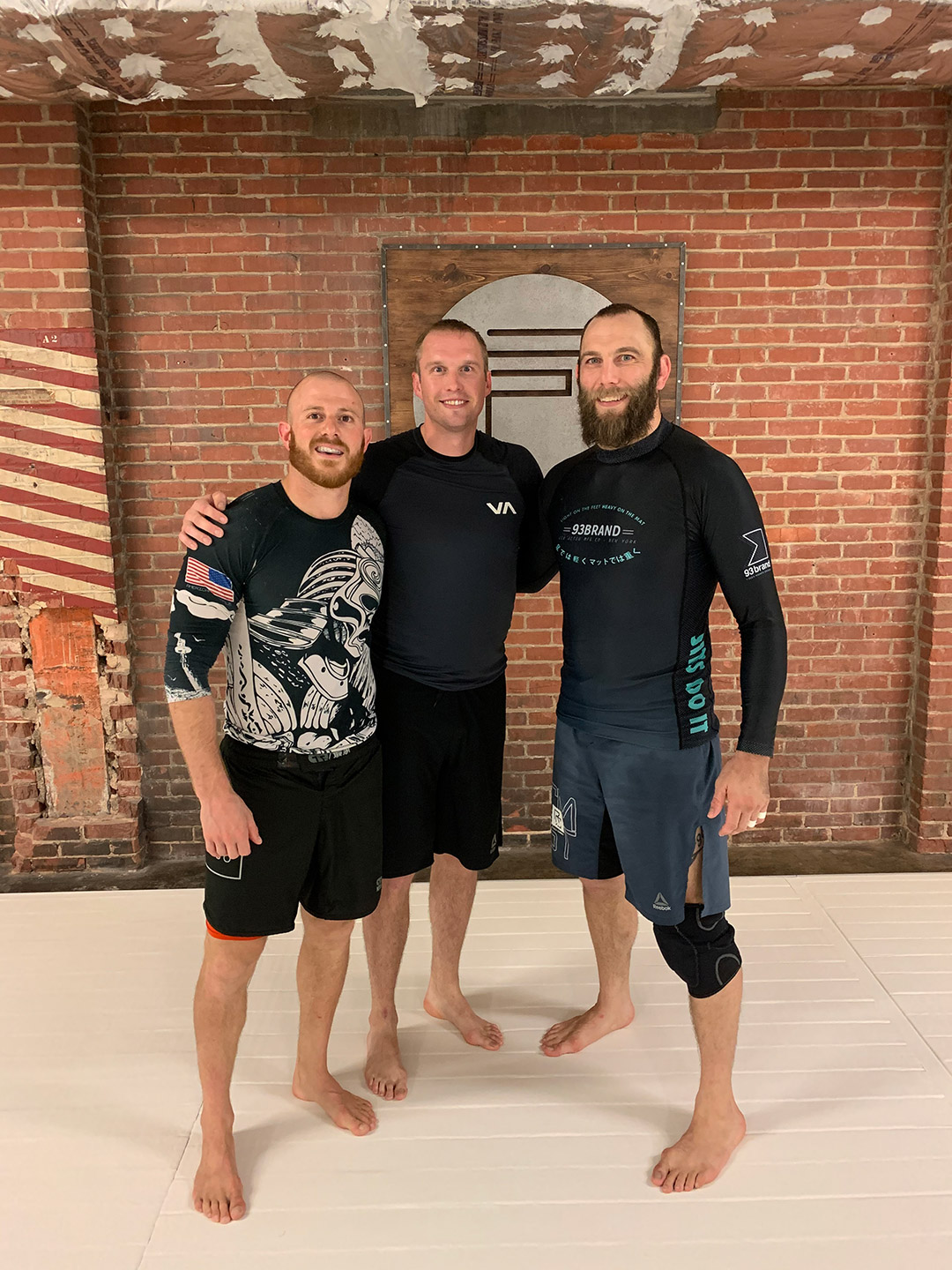 three men stand together in workout apparel.