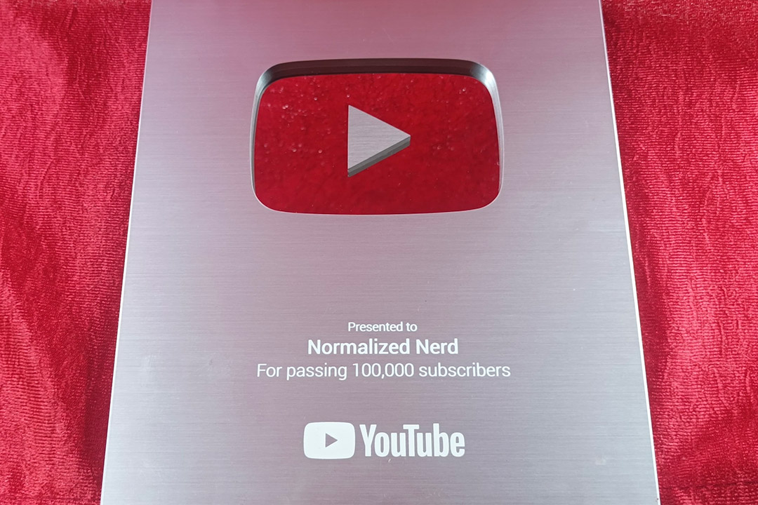 A silver plaque from YouTube showing 100,000 followers for the Normalized Nerd channel is shown.